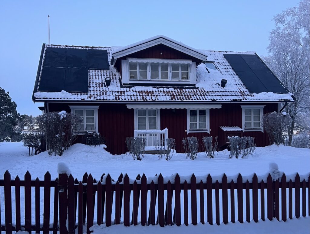 Solceller på taket av en röd villa i vinterlandskap. Solceller vars energi används för eget bruk.